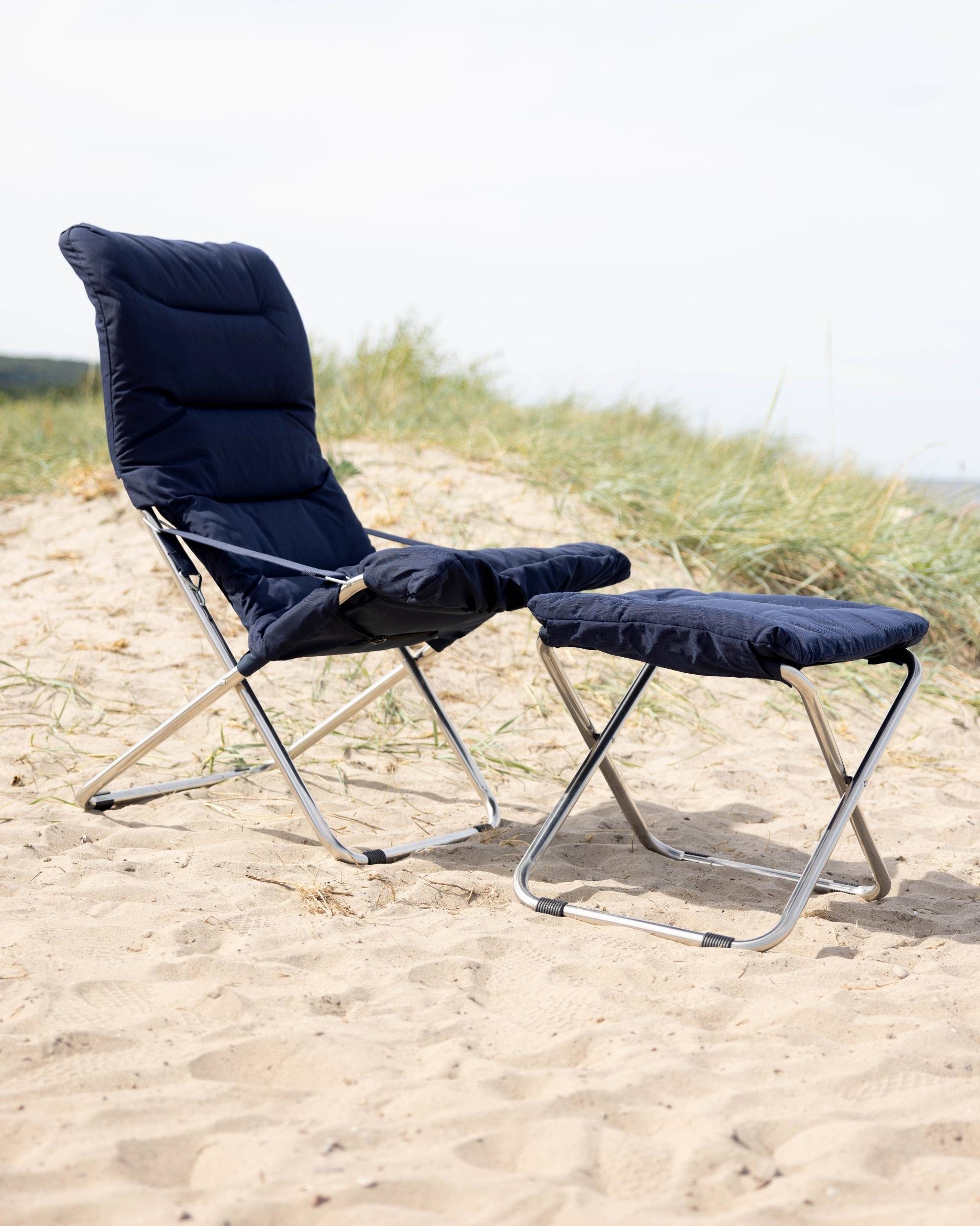 FIAM Chico Soft fotskammel med mørkeblå polstret pute og lett aluminiumsramme på sandstrand.