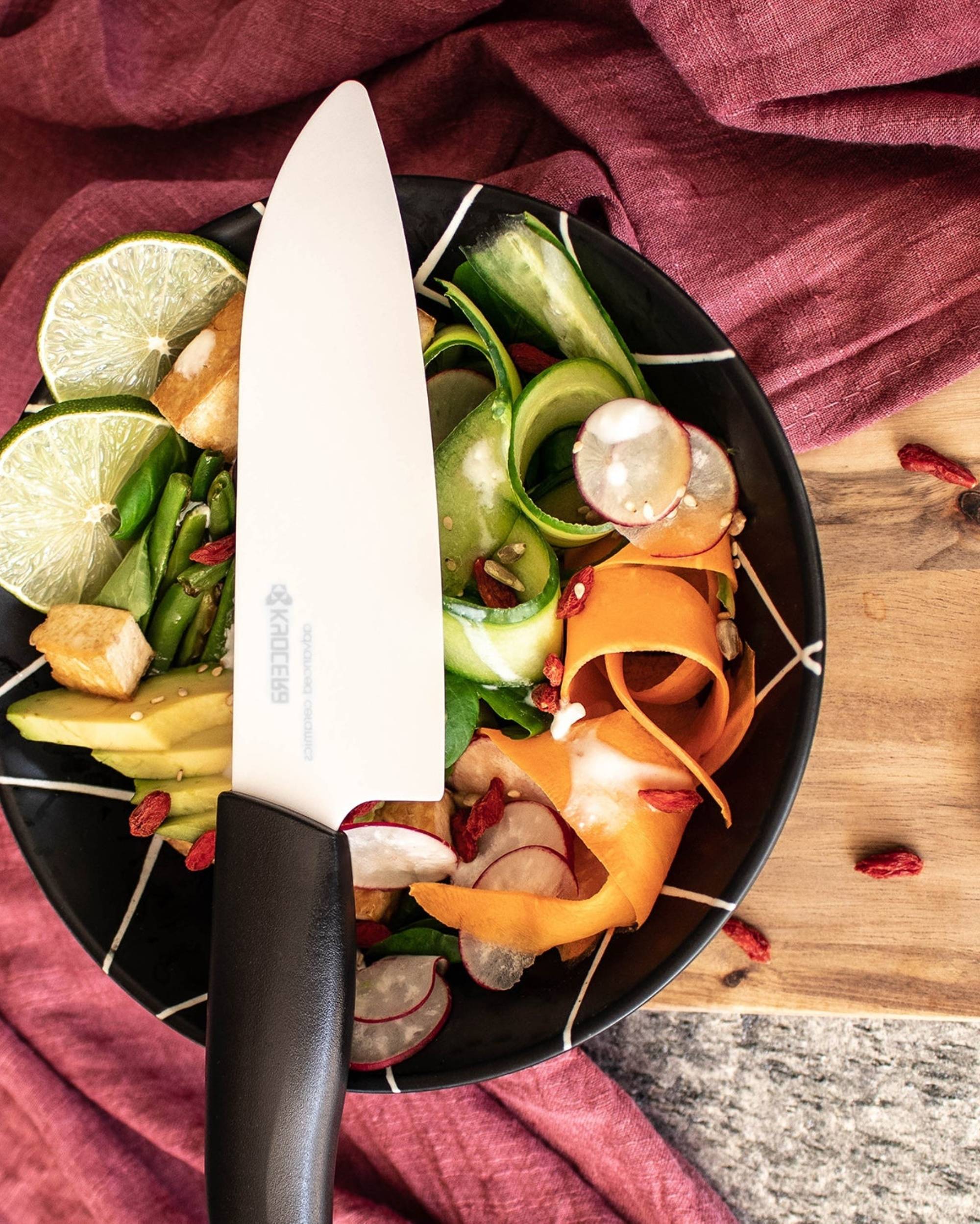 Kyocera BIO keramisk kokkekniv med hvitt blad og sort sukkerrørhåndtak, vist i salatbolle med lime og grønnsaker