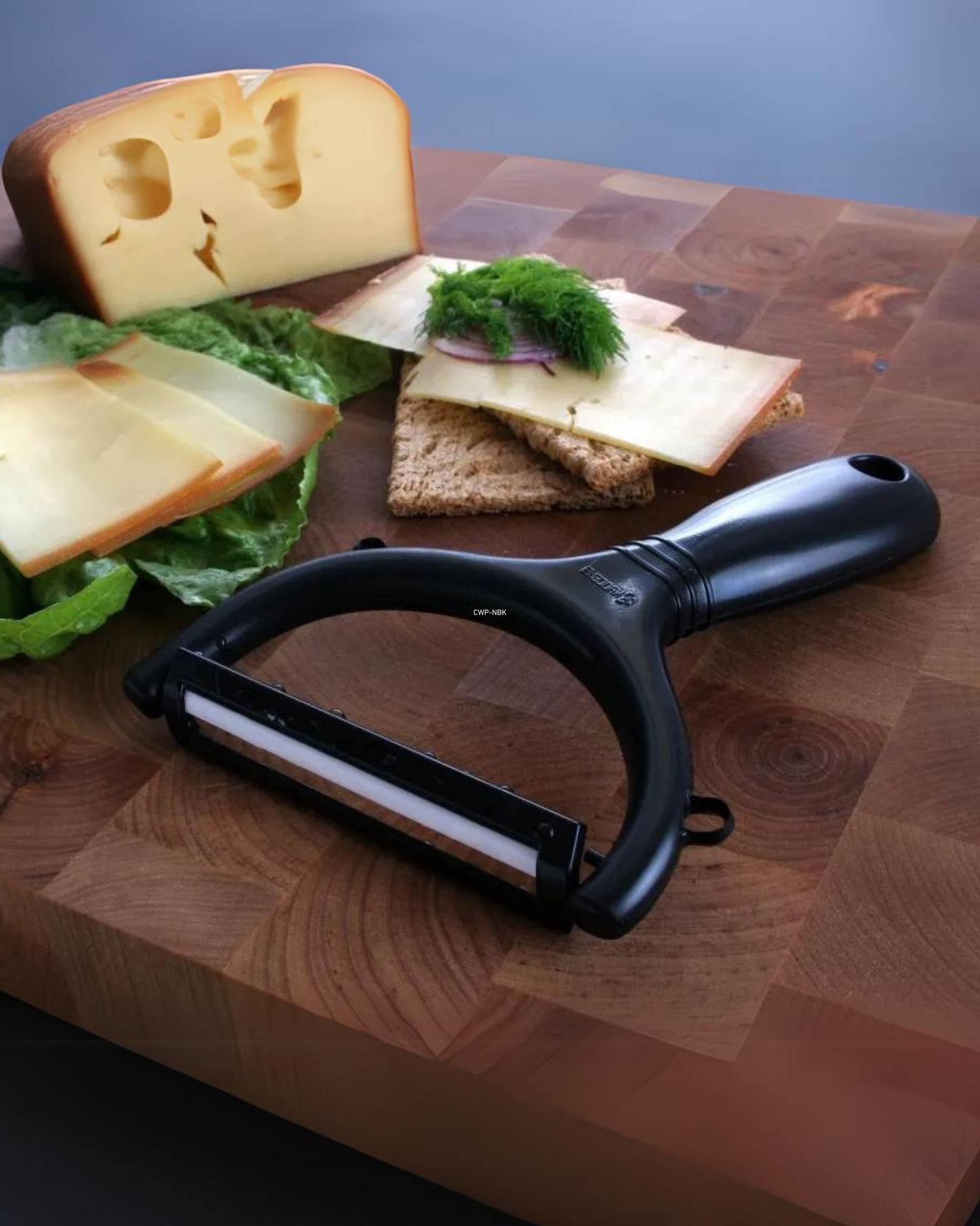 Kyocera skreller med svart håndtak og hvitt keramisk blad, ligger på et treunderlag med ost