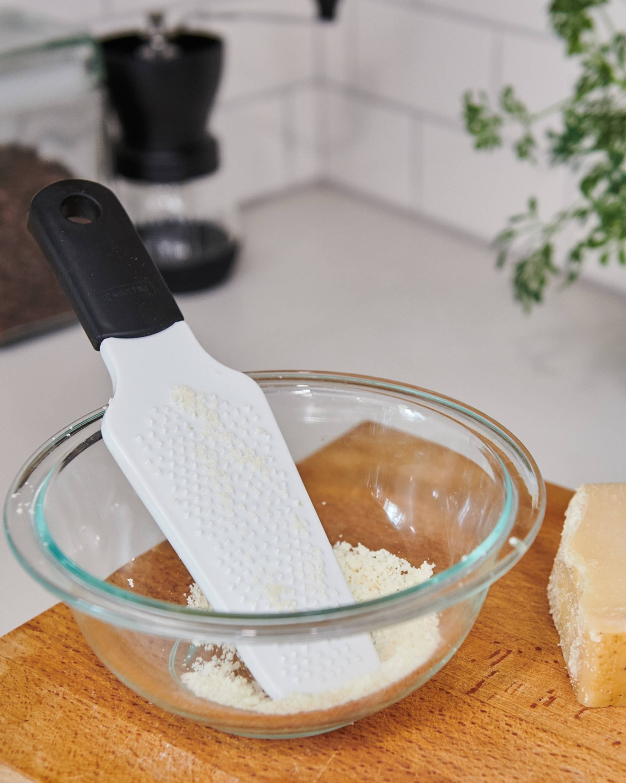Kyocera rivjern i hvit med sort grep, revet parmesan i glassbolle på trekuttbrett, kjøkkenkontekst