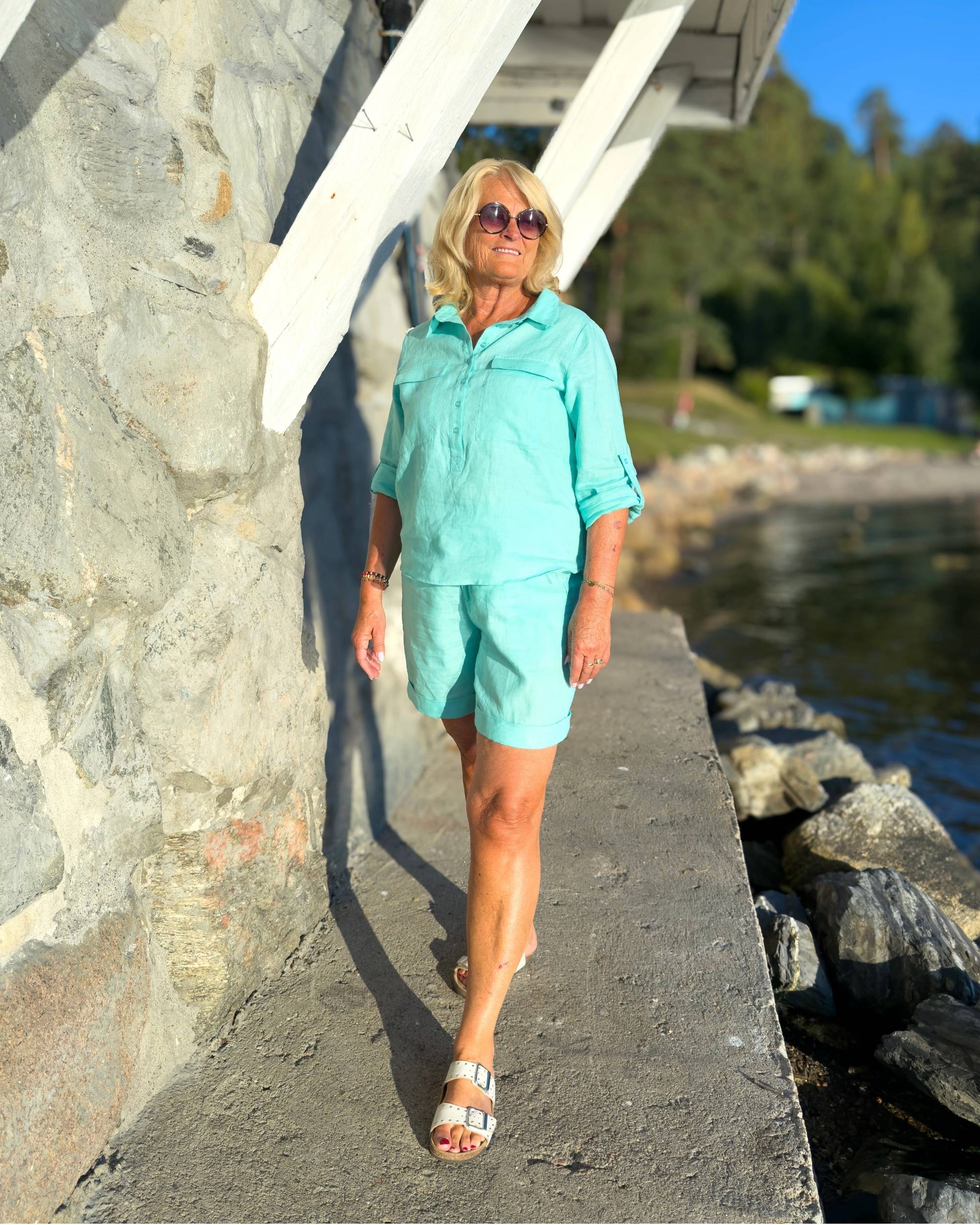 Close to My Heart Lacy Shorts i mintgrÞnn lin pÄ modell, med oppbrett og flettebelte, stÄende ved vannet i solskinn