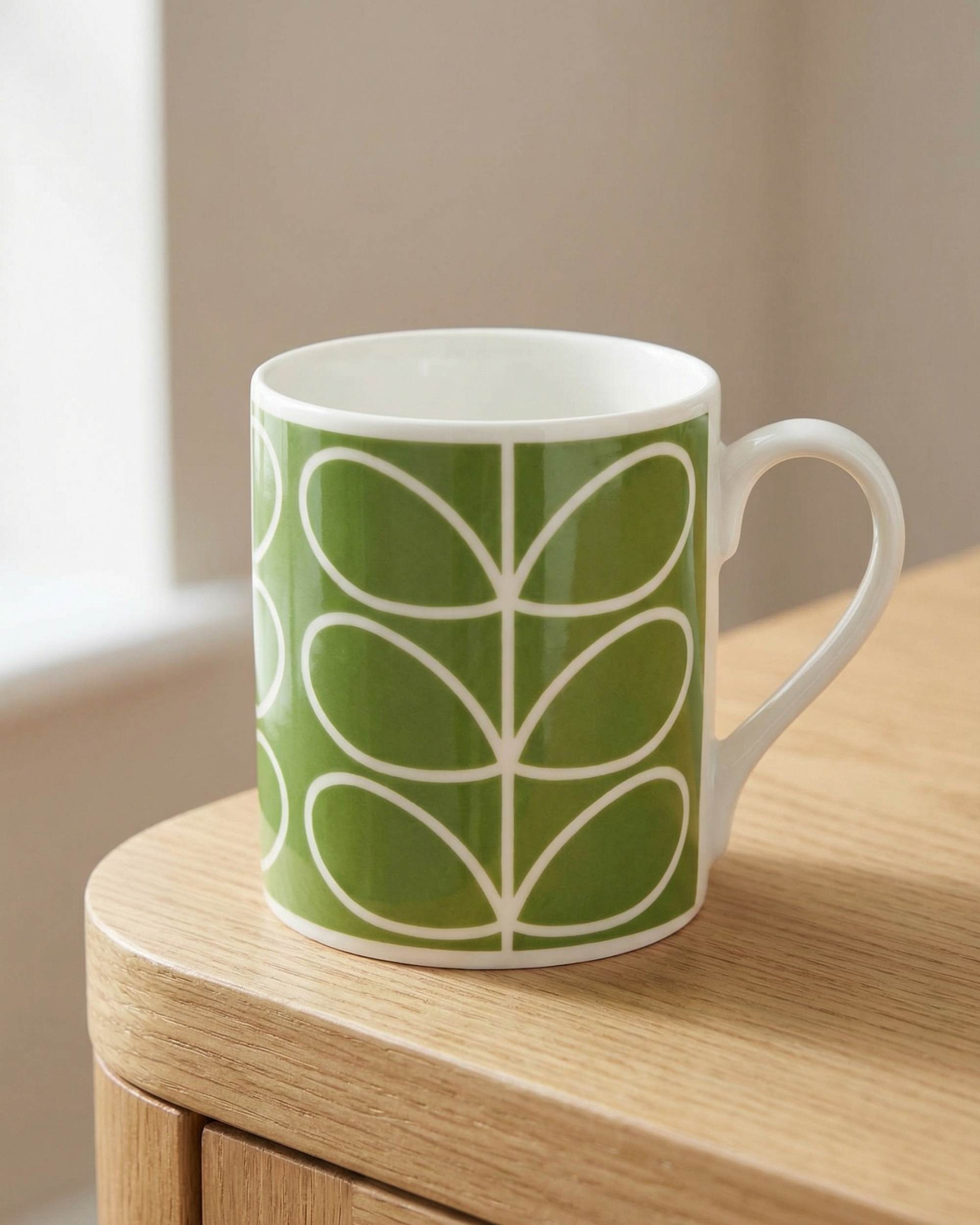 Orla Kiely Linear Stem Green kopp i grønn og hvit keramikk med stilrent bladmønster, hvit hank på treflate