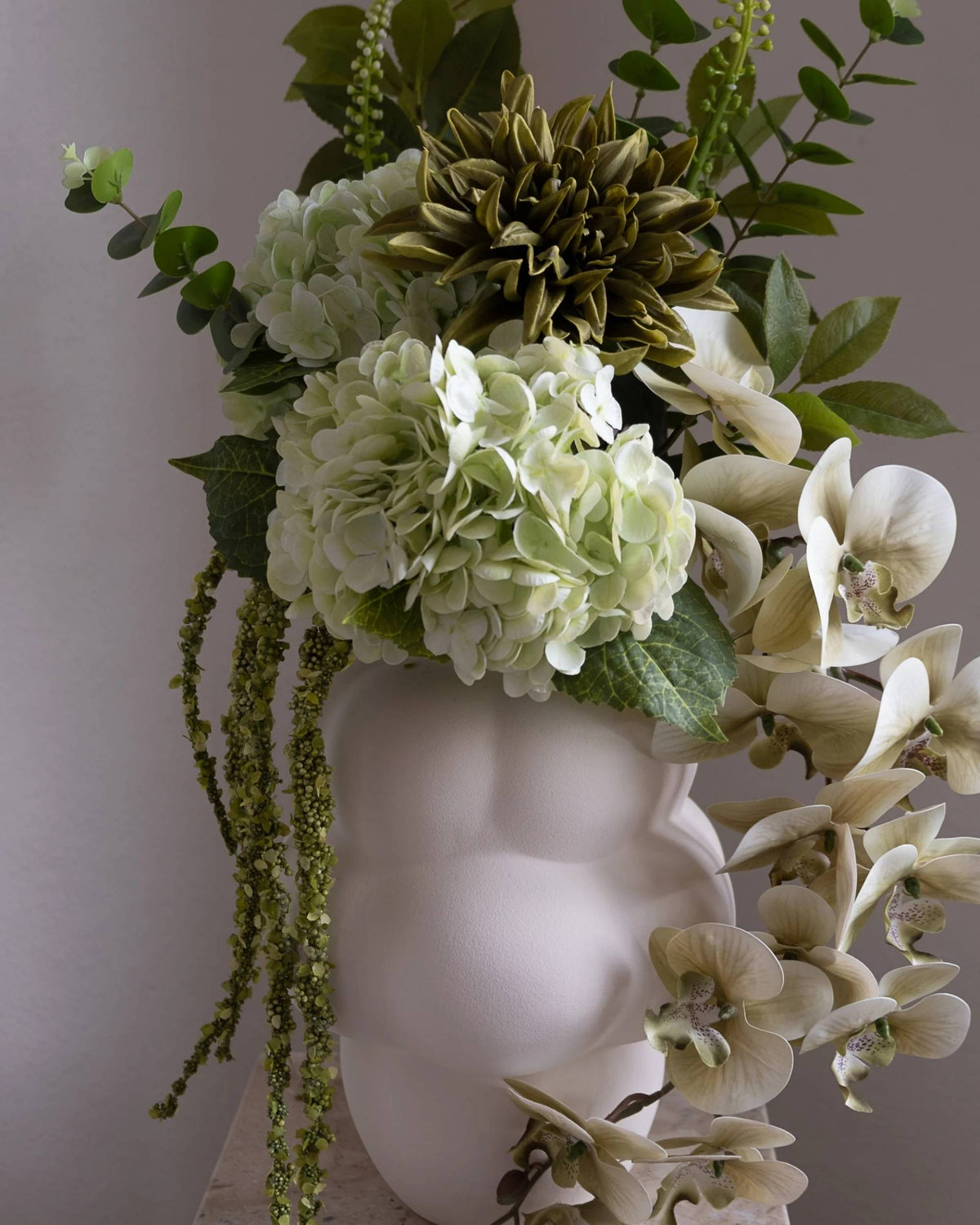 Detalj av Amarante Moss Field bukett fylt i hvit vase, med grønne hortensia, mosegrønne grener og kremfargede orkideer
