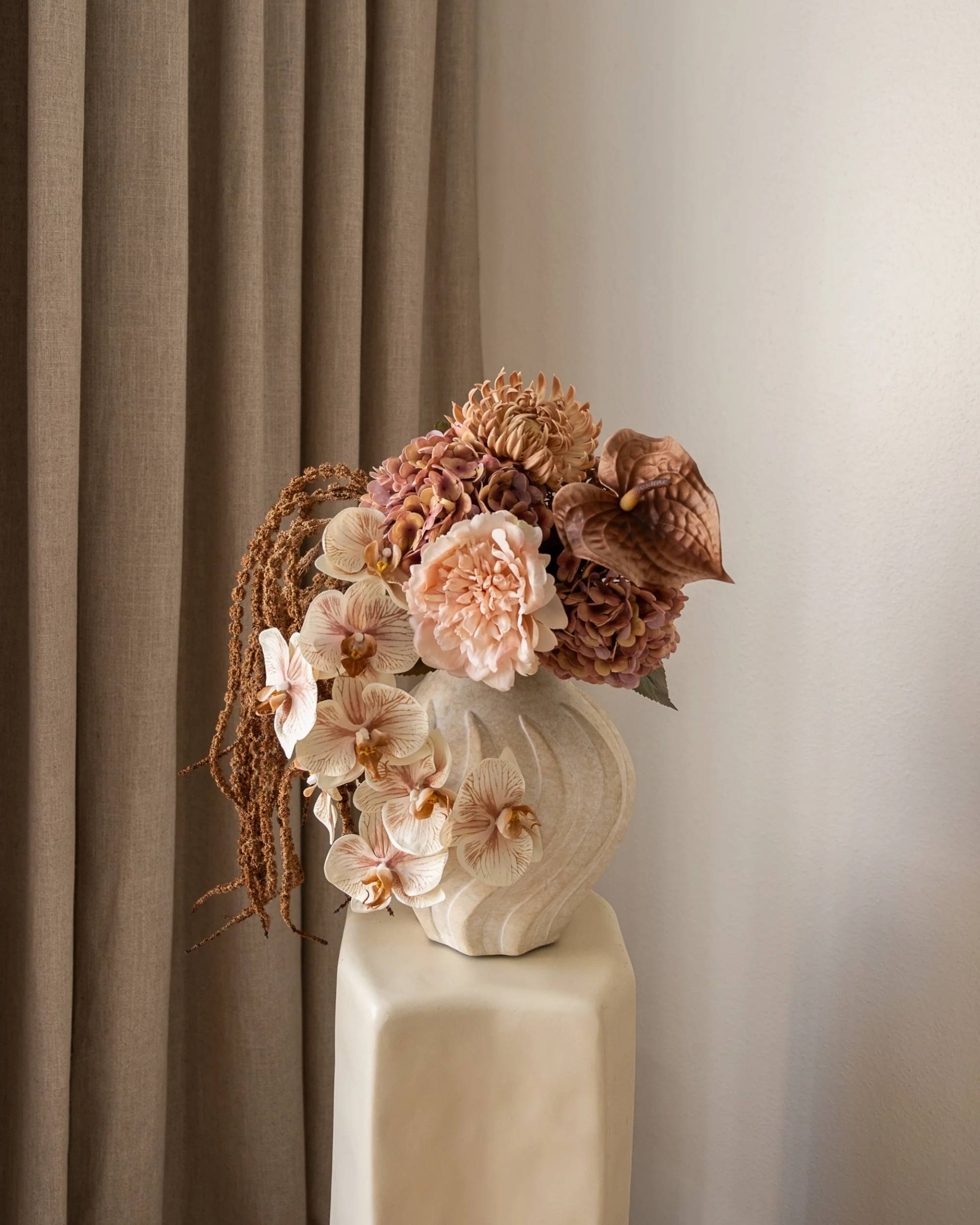 Amarante Rose Latte bukett med orkideer, peoner og anthurium i nyanser av kremrosa, beige og brunt i riflet vase