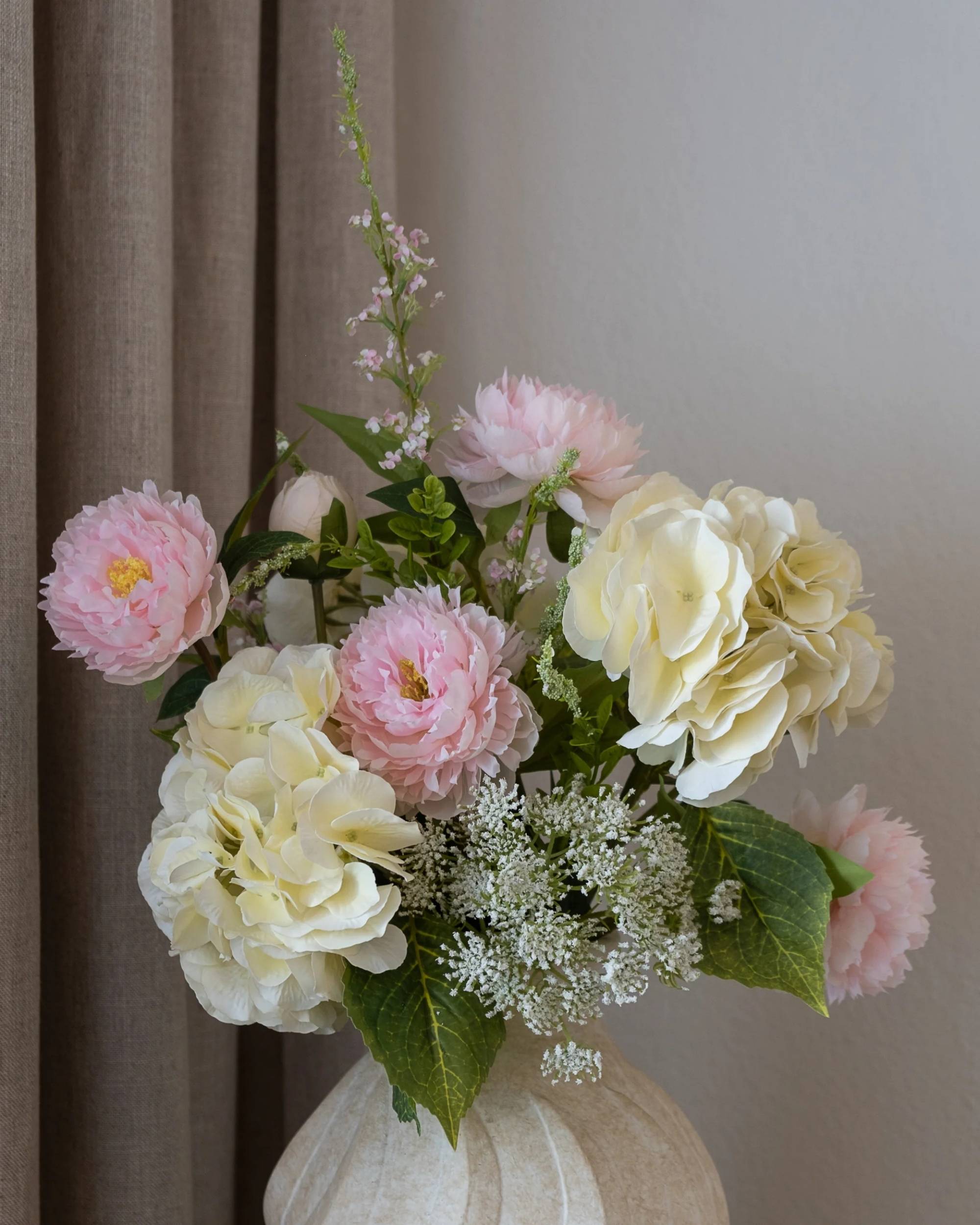 Strawberry Creme bukett: Detalj av rosa peoner, kremhvite hortensia-lignende blomster i lys strukturert vase