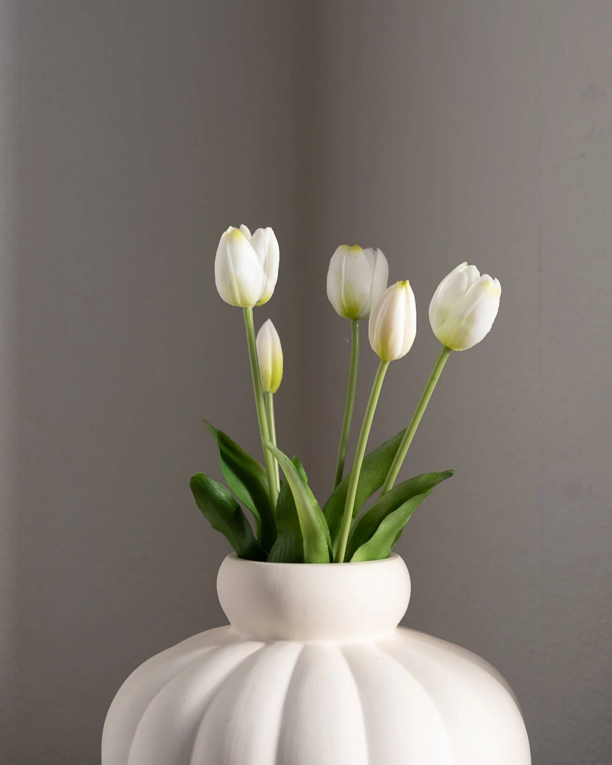 Amarante hvite kunstige tulipaner i en hvit vase med detaljert, riflet tekstur, mot en grå bakgrunn.
