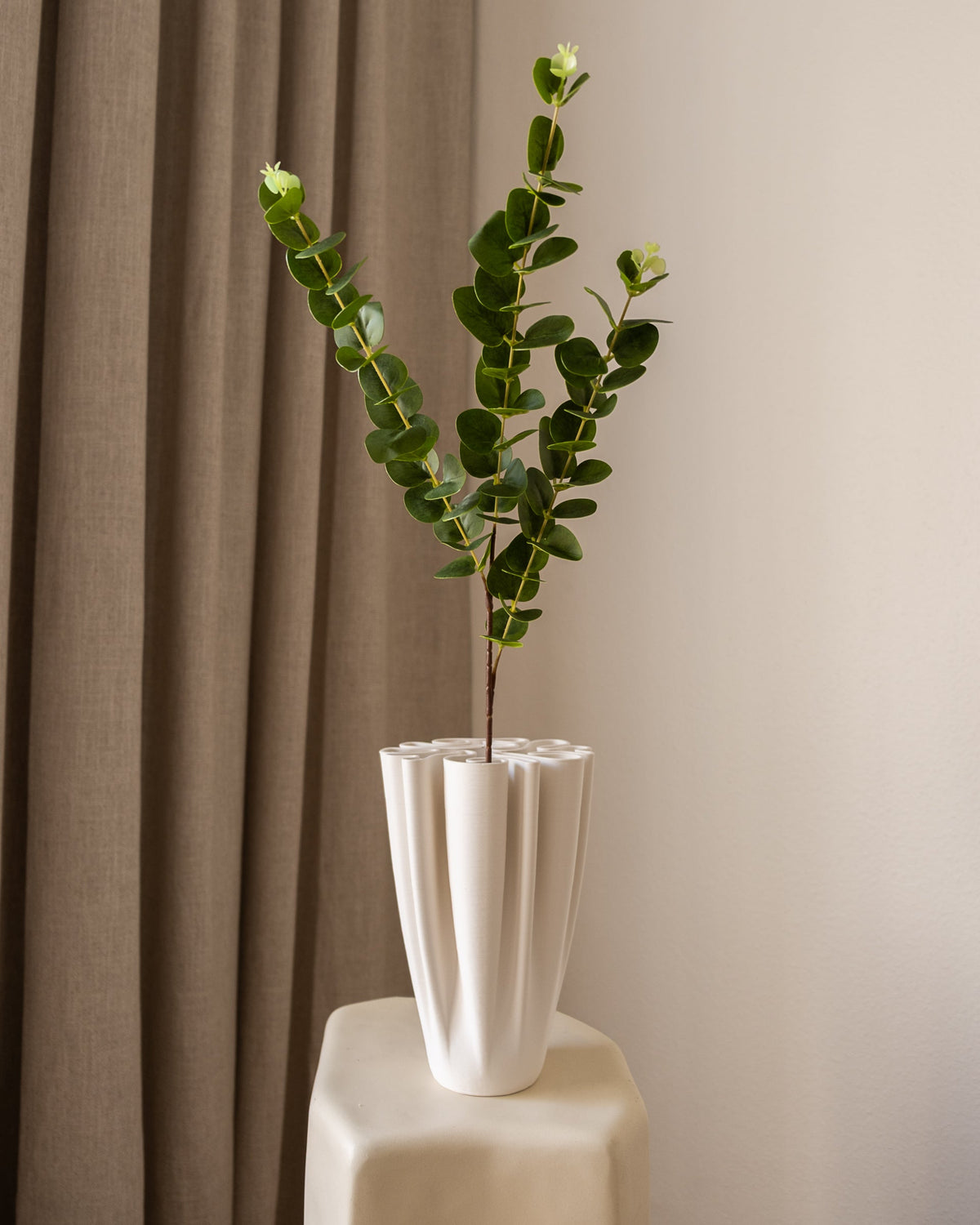Amarante Eucalyptus Gren, grønn kunstig blomst med runde blader, i en hvit riflet vase på en beige sokkel