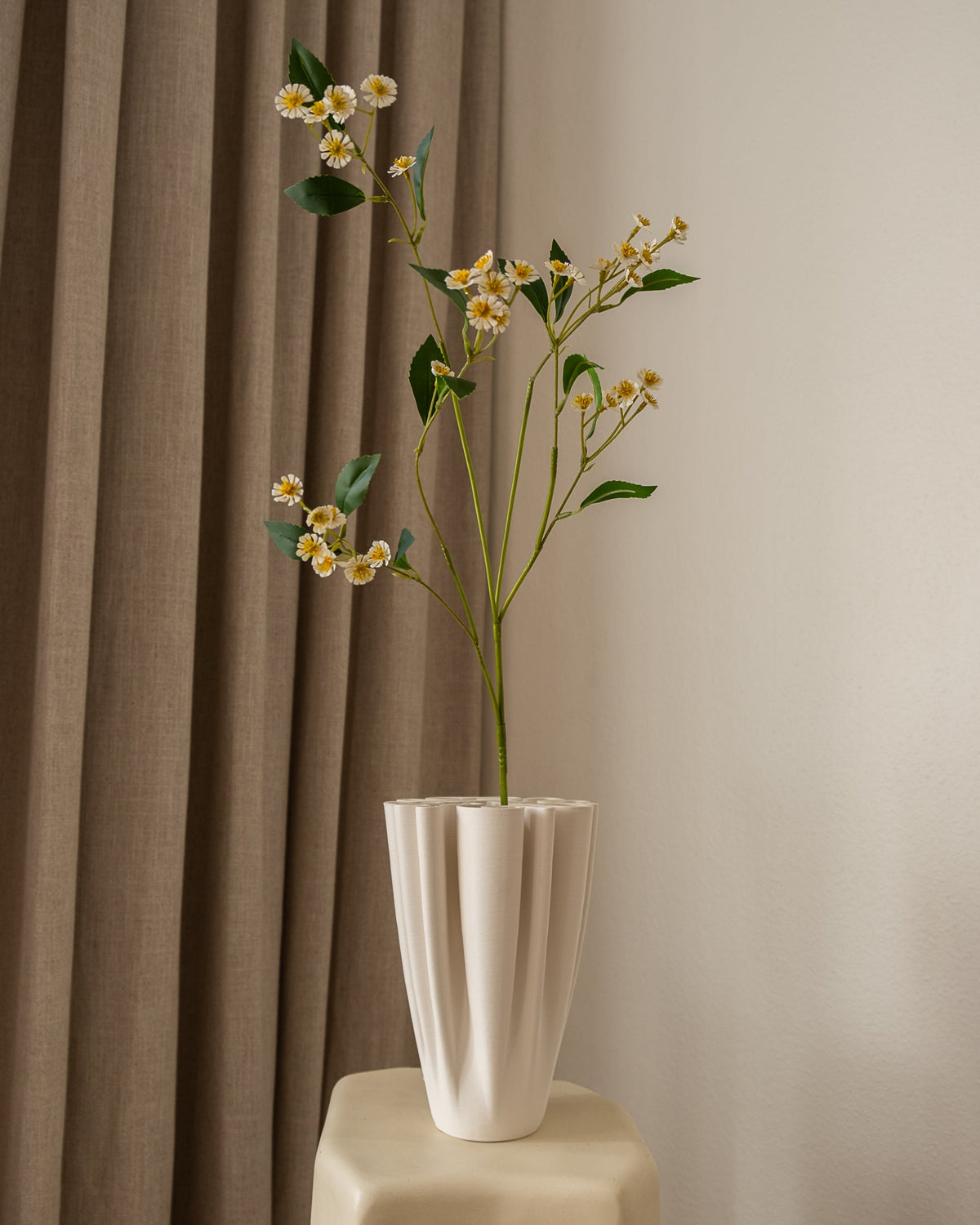 Amarante kunstig Chamomile Daisy med hvite og gule blomster, i en hvit riflet vase, foran brune gardiner.