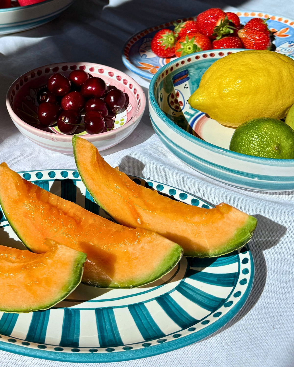 Dipinto Linea Ovalt Fat 24cm med håndmalt turkis-stripet mønster, tre skiver melon ligger på fatet