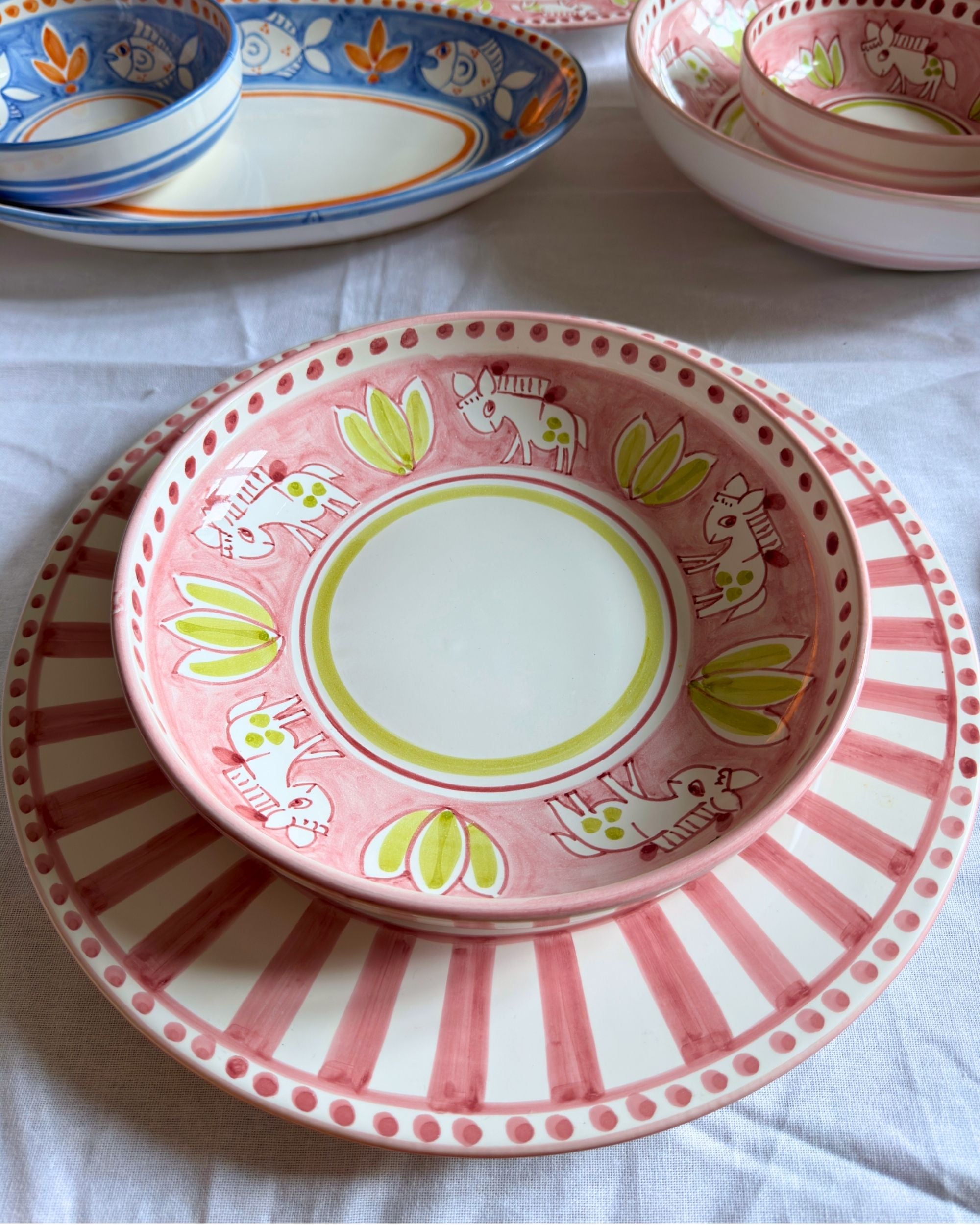 Dipinto Linea Rundt Fat keramikkfat i rosa og hvitt med håndmalte striper, spenstige hestemotiver og grønne blader.