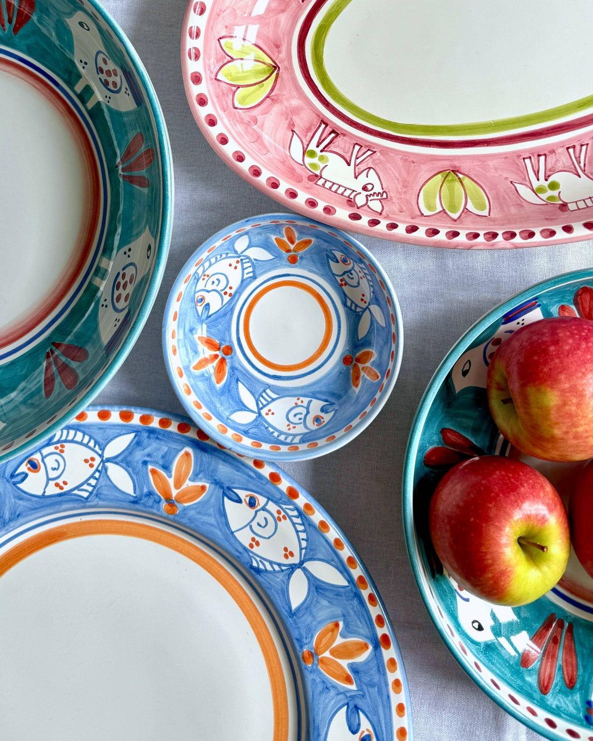 Dipinto Ceramics Amalfi Liten Bolle 13cm med håndmalt blått fiskemønster og oransje detaljer, omgitt av liknende servise.