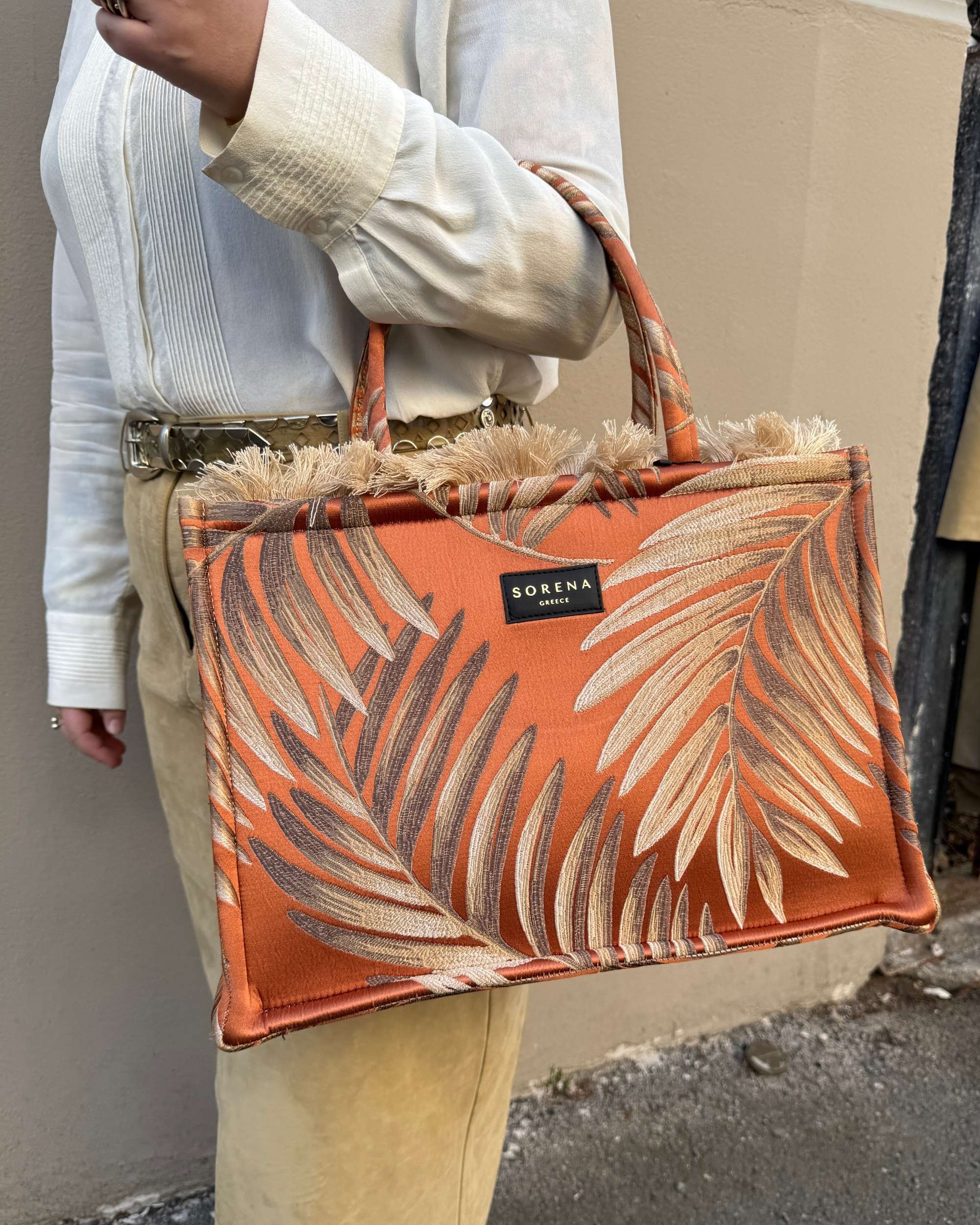 Modell med Sorena Ftera Large Tote Bag i oransje brokade med palmeblader og frynser, bæres i hånden