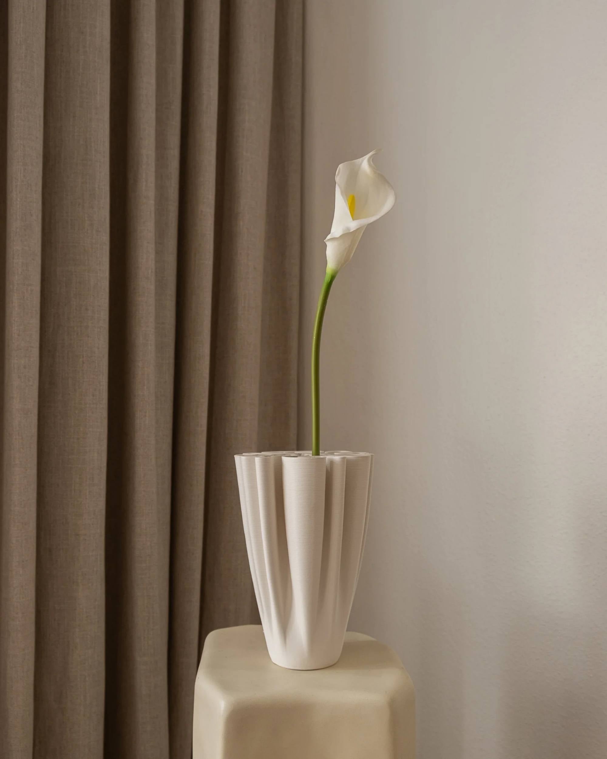 Amarante Calla Lilje i hvit, kunstig blomst med grønn stilk og gul midte i hvit plissert vase på kremfarget pidestall