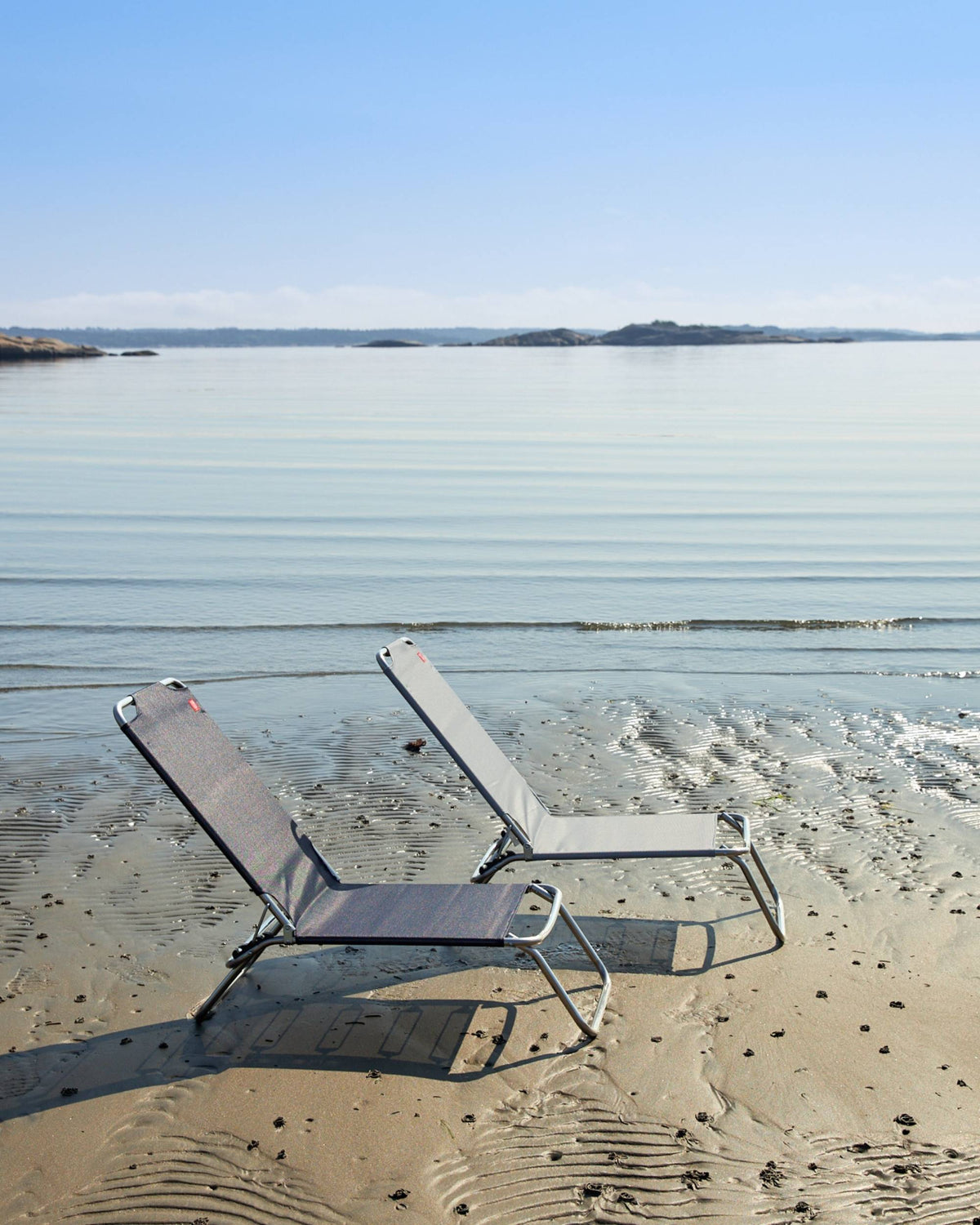 Fiam Jolly strandstol, sett bakfra, mørk og lys grå texfil-tekstil, aluminiumsramme på en strand ved vannet