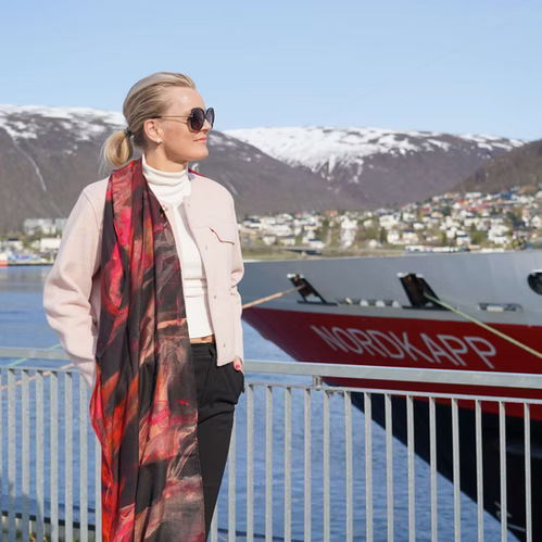 Movement skjerf fra Therese Enger med abstrakt mønster i rødt, sort og oransje, drapert over hvit genser utendørs
