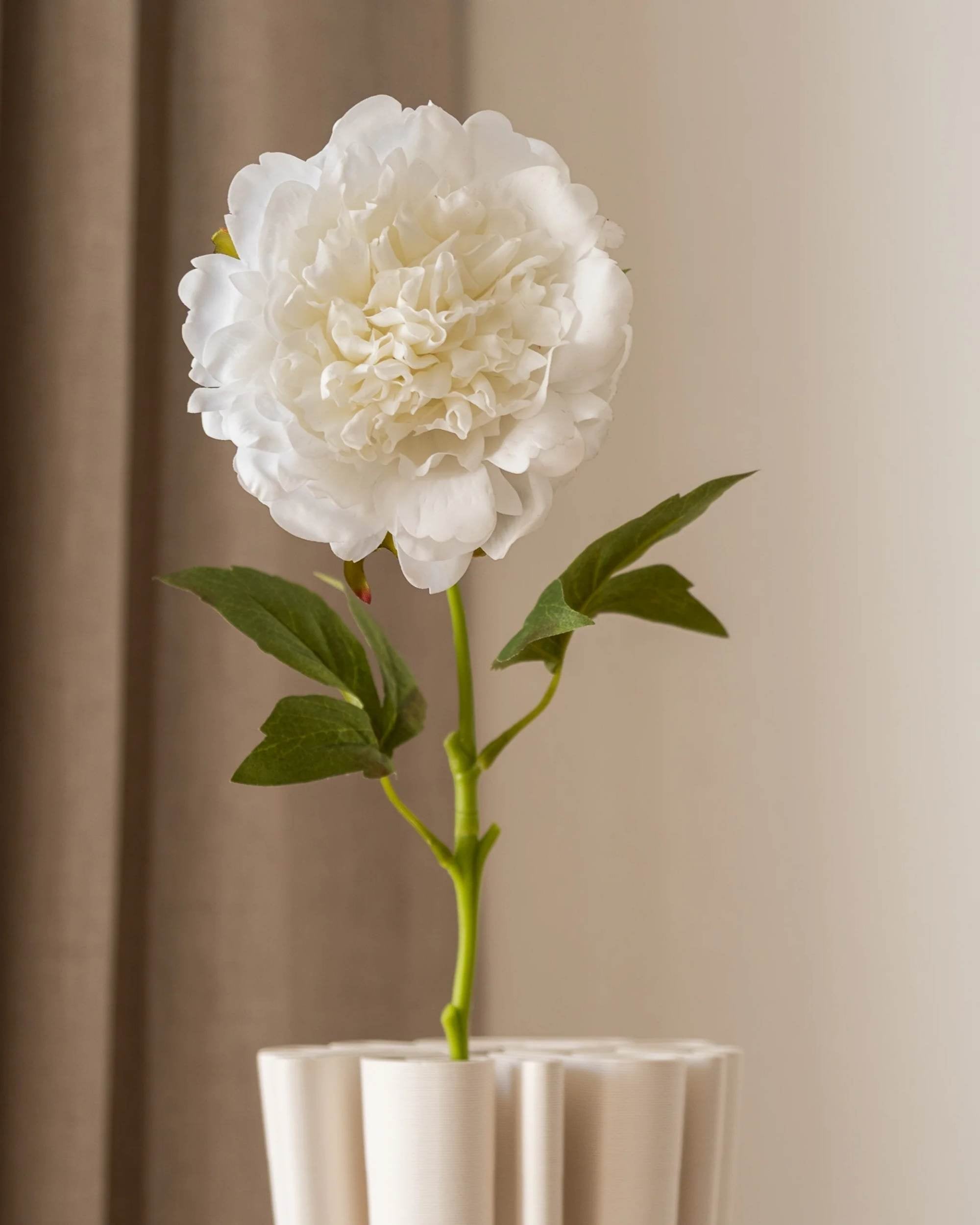 Amarante Peon i helfigur, hvit og elegant kunstig blomst med grønne blader, står i en lys vase.