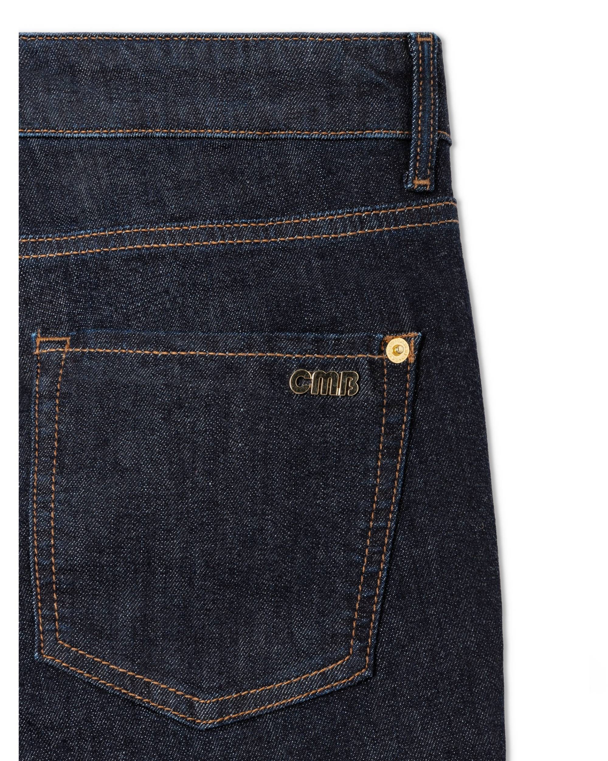 Detalj av Cambio Piper Long bukse i mørkeblå denim med oransje sømmer og gullfarget CMB-logo ved baklommen.