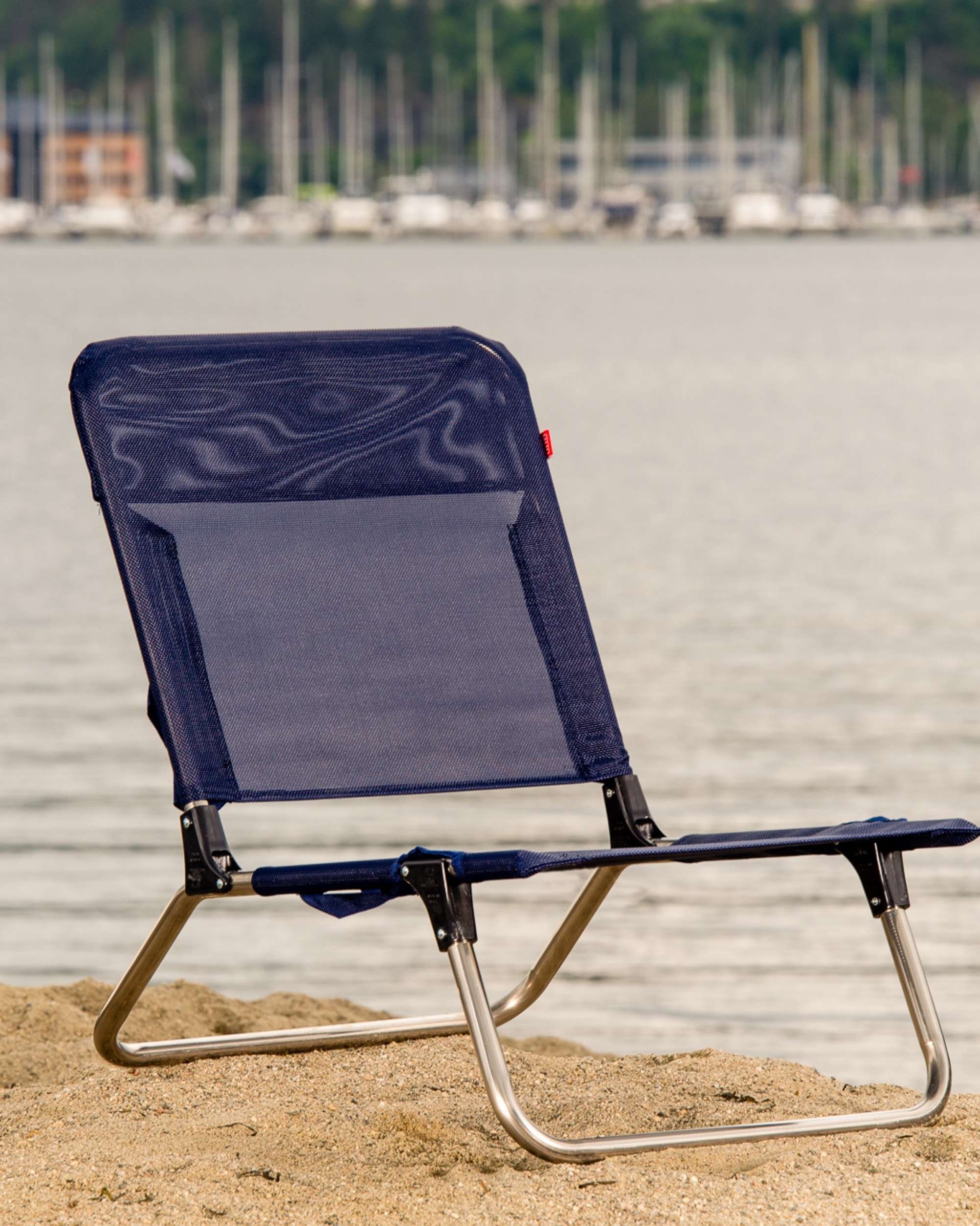 FIAM Quick strandstol i mørkeblå meshstoff og aluminiumsramme, sett fra siden på en sandstrand ved vannet