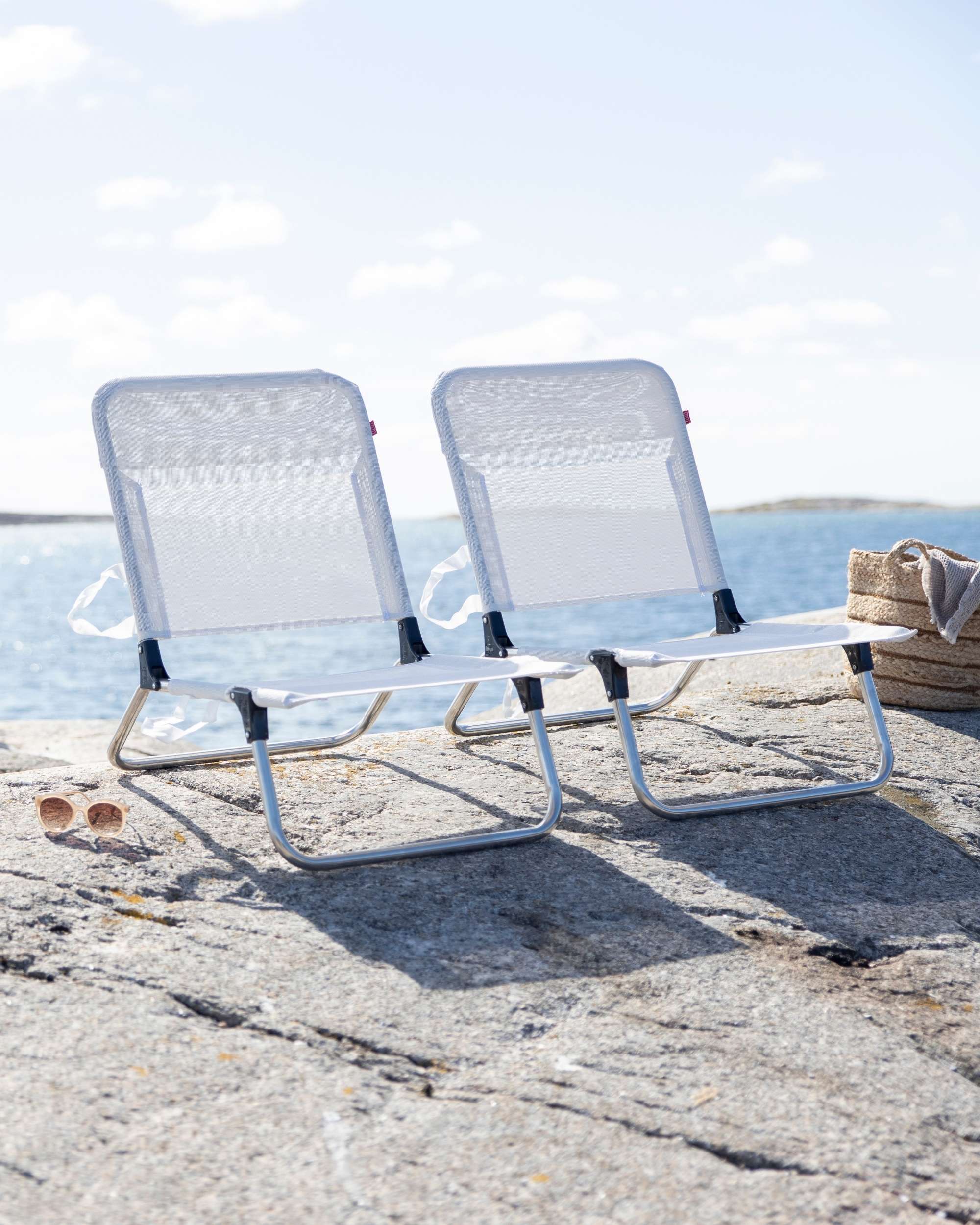 To hvite Fiam Quick strandstoler på en solrik fjellknaus ved sjøen, nær bakkenivå