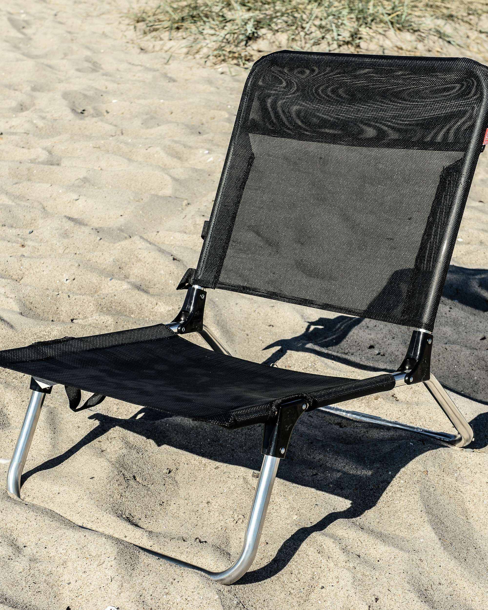 Fiam Quick strandstol i svart mesh-stoff med sølvfarget aluminiumsramme, står på sandstrand