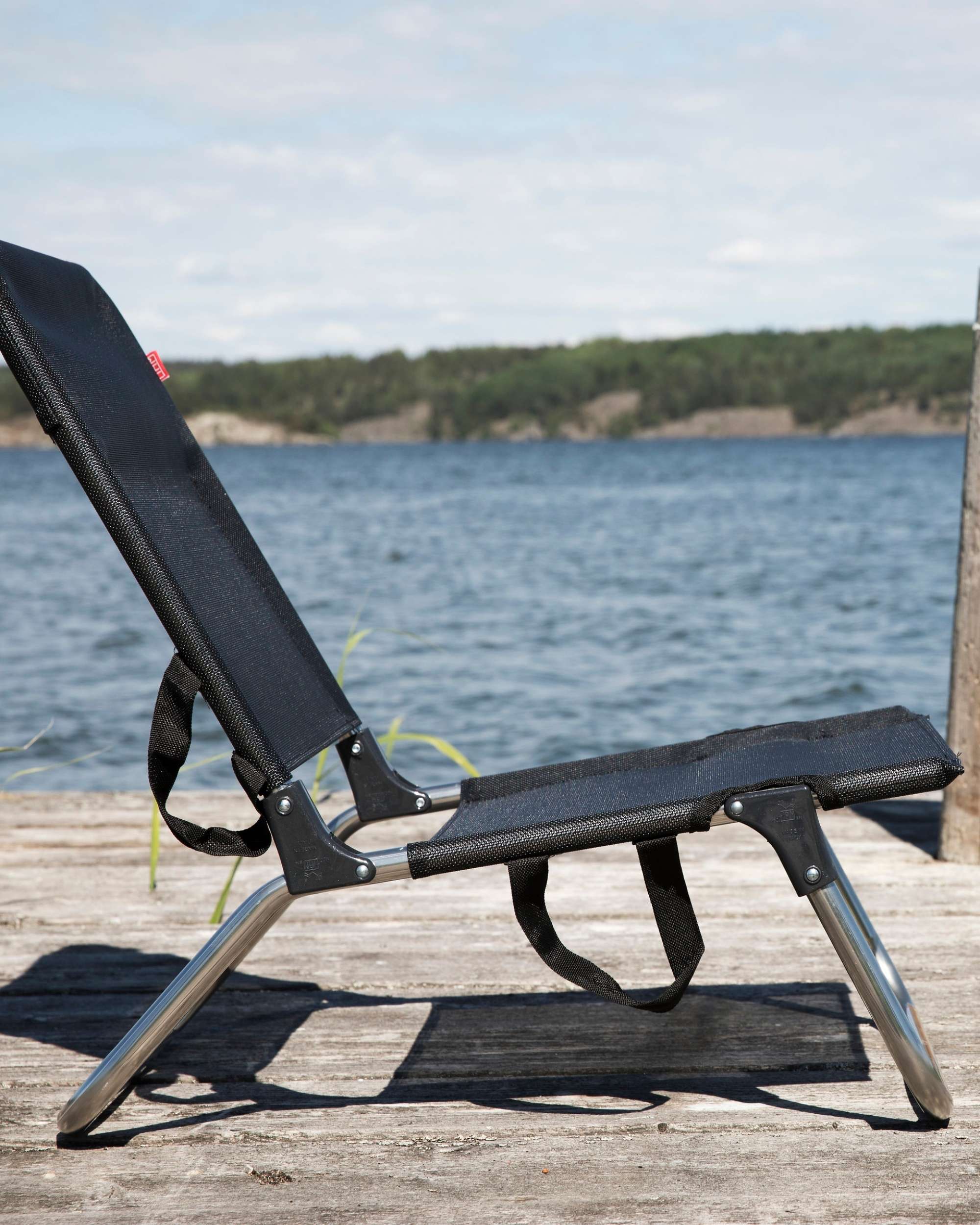 FIAM Quick strandstol i svart tekstil og aluminium, med bærehåndtak på brygge ved vannet