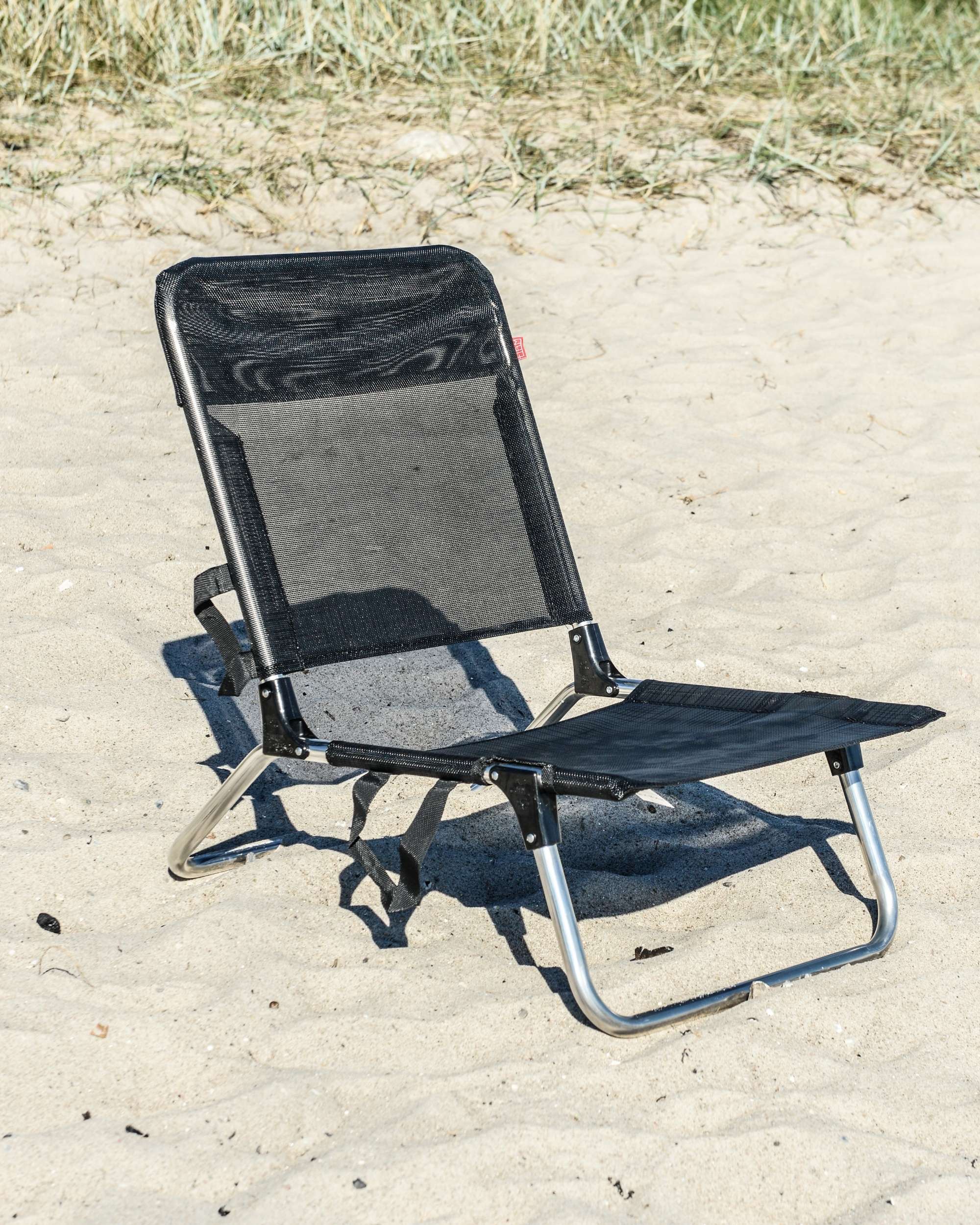 Fiam Quick strandstol, detaljbilde med justerbart ryggstykke i svart tekstil og aluminiumsramme på sandstrand