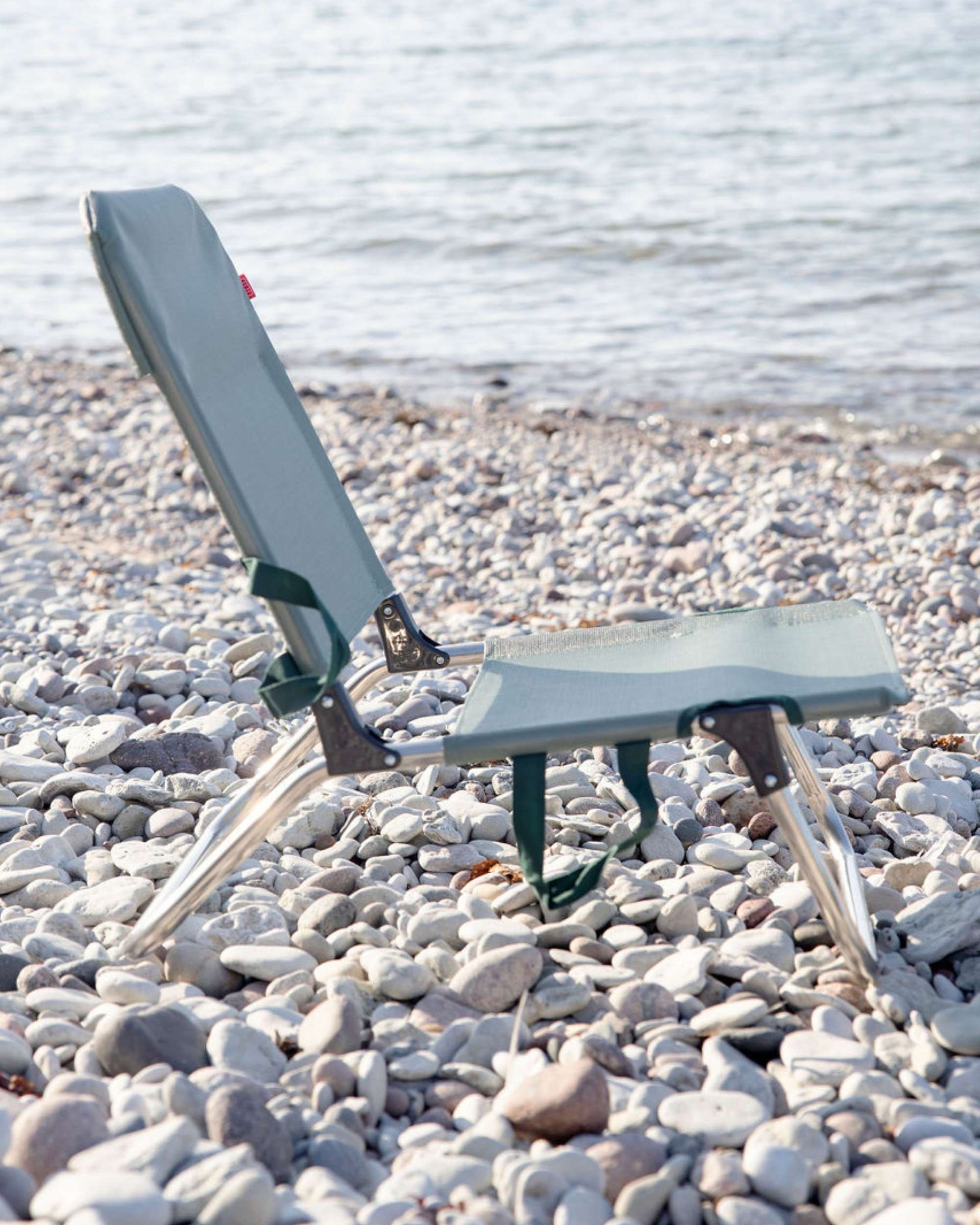 FIAM Quick strandstol, detalj av aluminiumsrammen og grønt slitesterkt stoff på rullestein ved sjøen