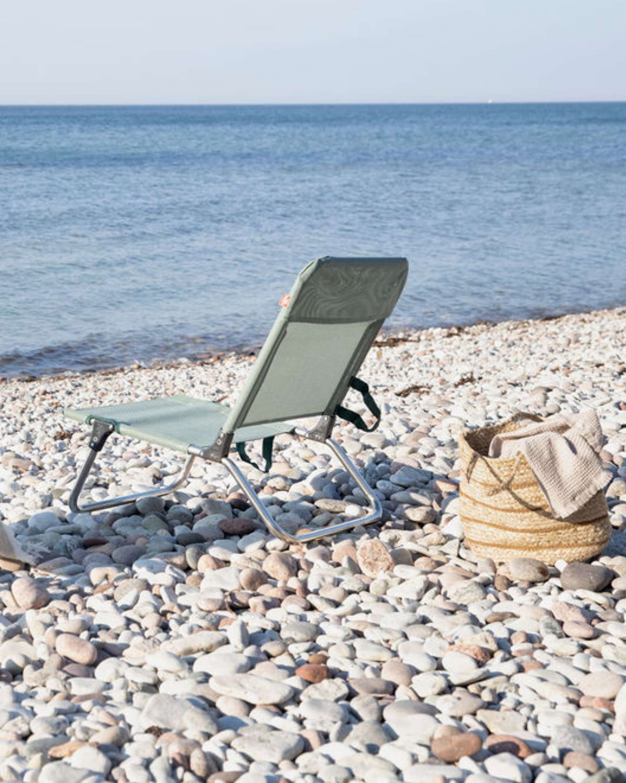 FIAM Quick strandstol i grønn, lett aluminiumsramme, sett fra siden på steinstrand ved sjøen