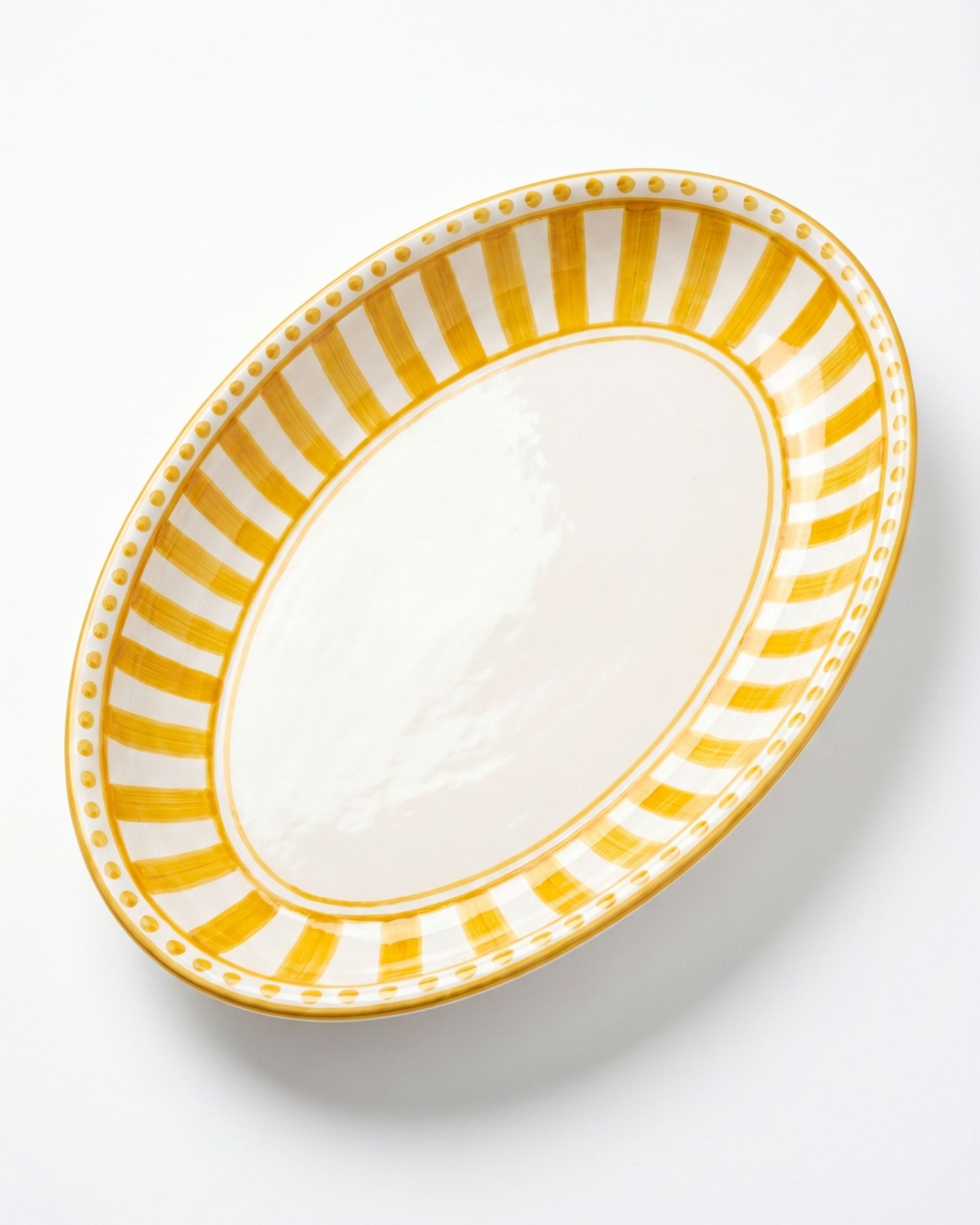 Linea Ovalt Fat fra Dipinto Ceramics. Kremfarget keramikkfat med gult stripemønster og prikkete kant langs kanten.