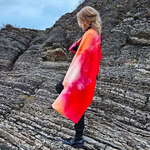Therese Enger Utopia kunstskjerf i silke/ull med abstrakt print i oransje og sterk rosa, på klipper ved sjøen