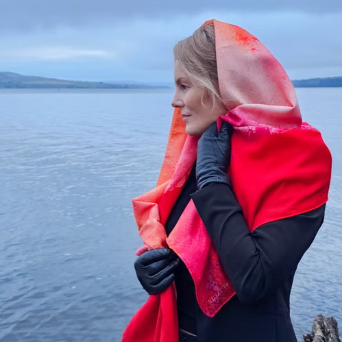 Modell med Therese Enger Utopia Kunstskjerf i rødt og oransje silke/ull med trykk, ved sjøen